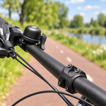 Sfeerbeeld op basis van leveranciersfoto: zwarte fietsbel met AirTag-houder op een fietsstuur bij een fietspad